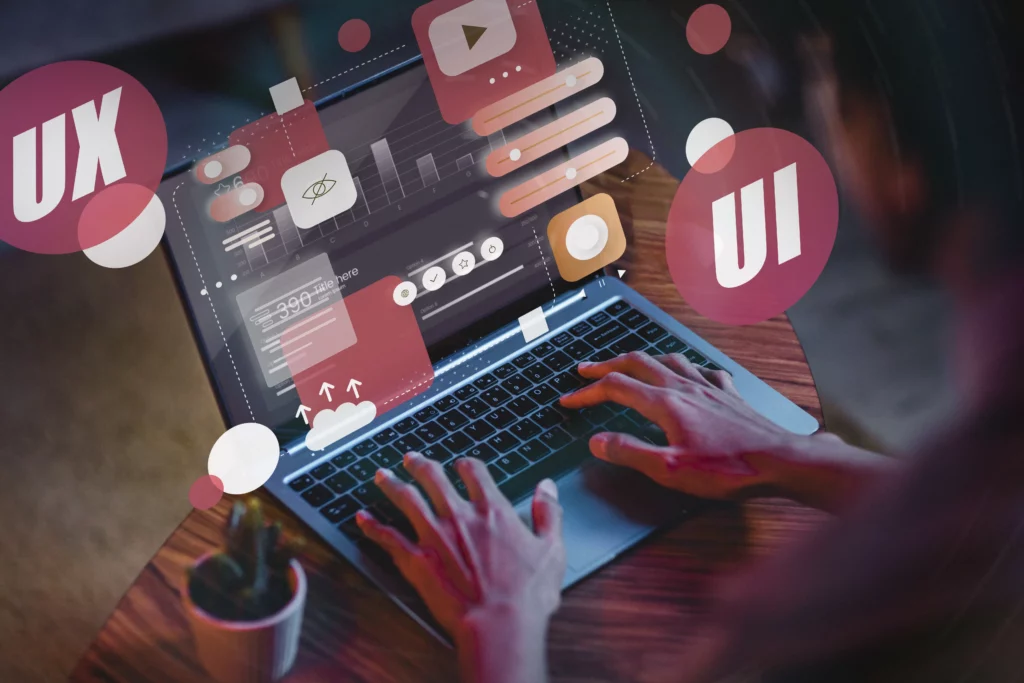 une personne en train d'utiliser un ordinateur. Des symboles ressortent de l'écran "UX", "UI", des barre de progression, etc