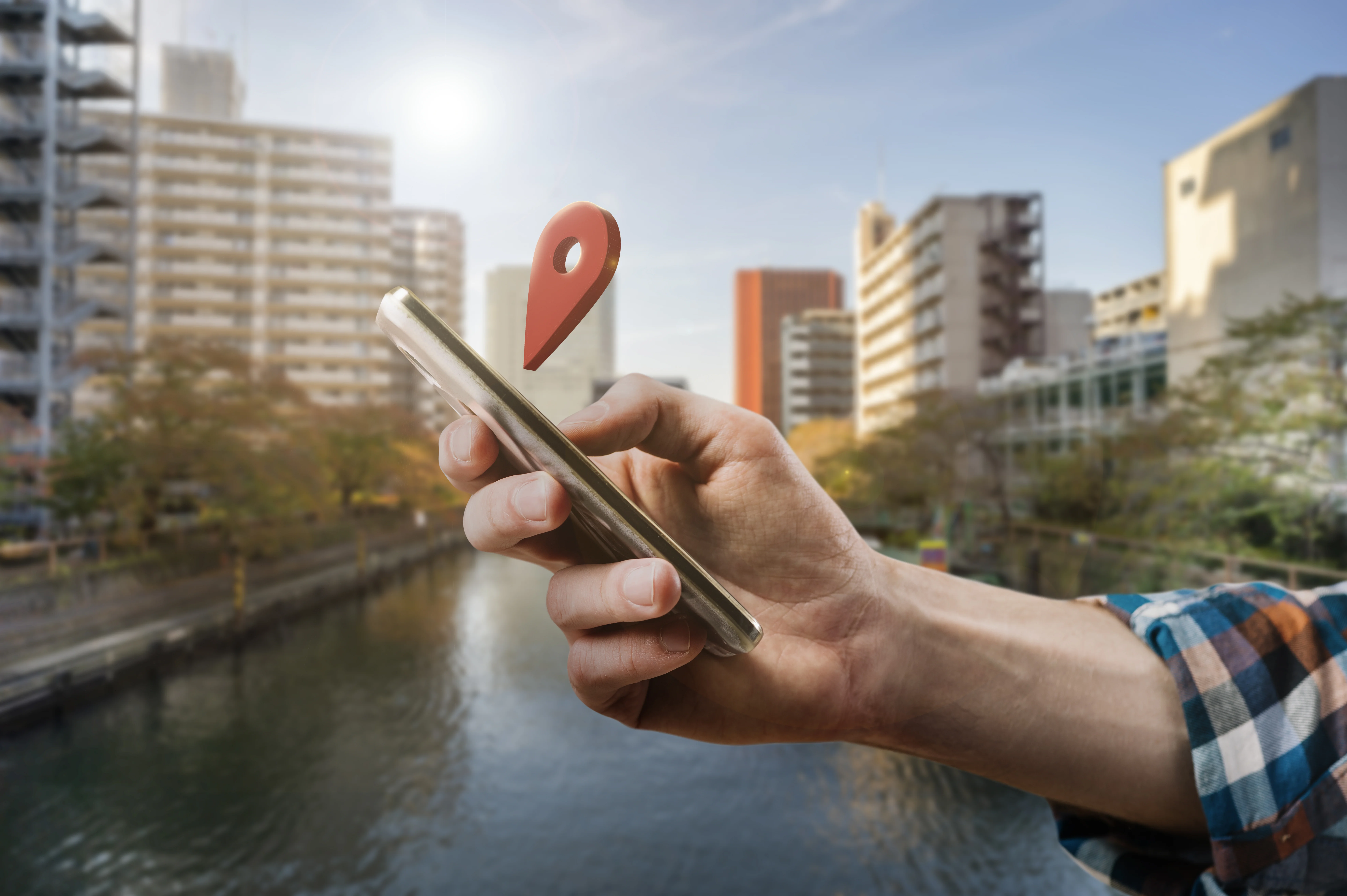 Une main avec un téléphone au-dessus duquel il y a un ping de position GPS et en fond une ville